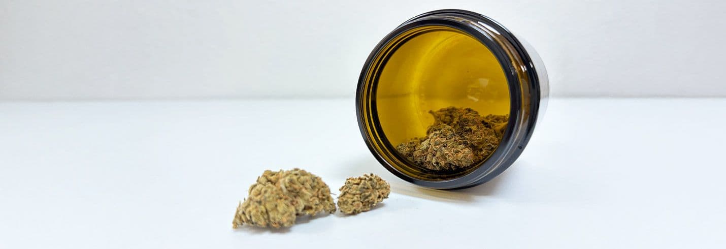 braunes Glas mit Cannabis Blüten vor weißem Hintergrund